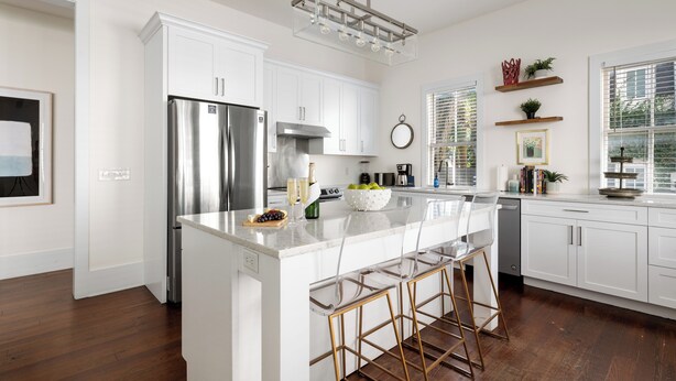 A modern kitchen with white cabinetry, a stainless steel refrigerator, a large island with bar stools, and a pendant light. - Luxurious Escape in Downtown Charleston | Apollo (Charleston)