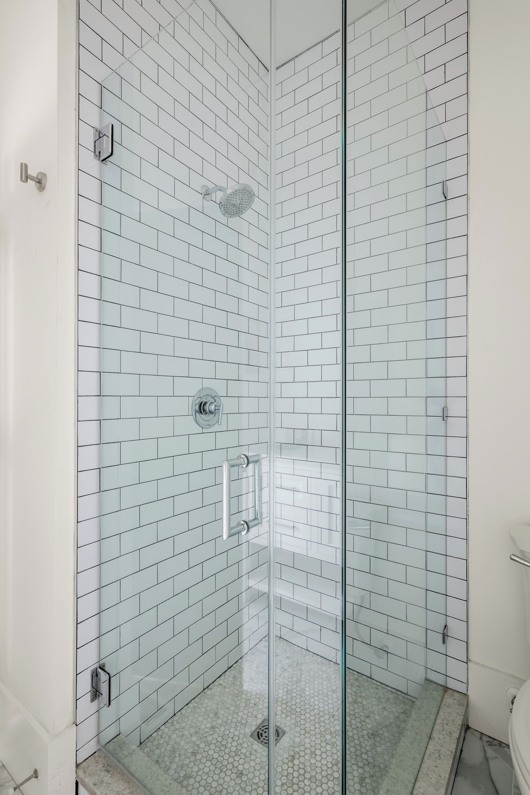 A modern bathroom with white subway tiles, a glass shower enclosure, and a toilet.