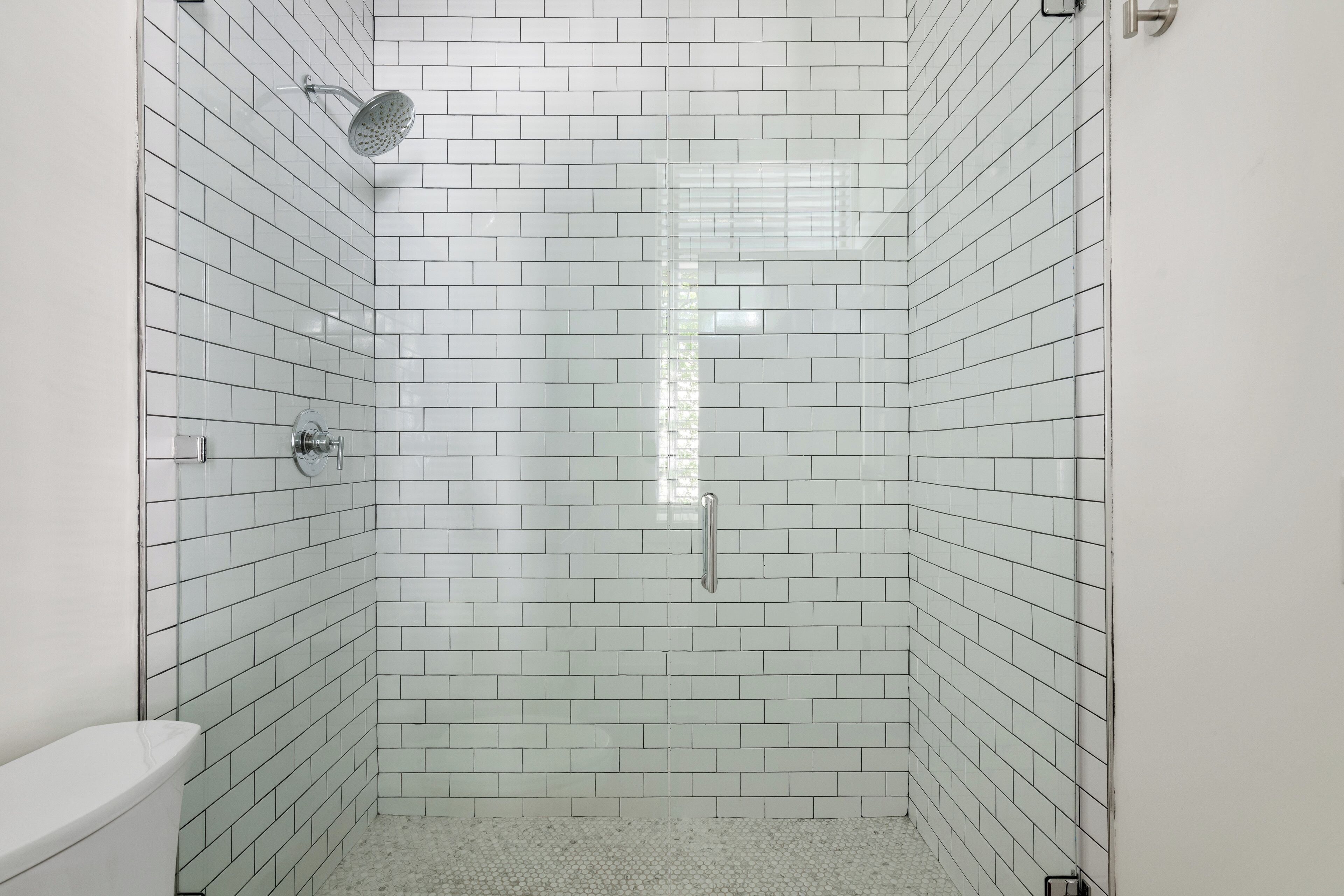 Un baño con azulejos blancos tipo metro, una ducha con cabezal de ducha manual y un inodoro.