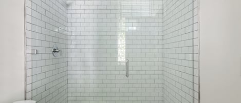 Un baño con azulejos blancos tipo metro, una ducha con cabezal de ducha manual y un inodoro.