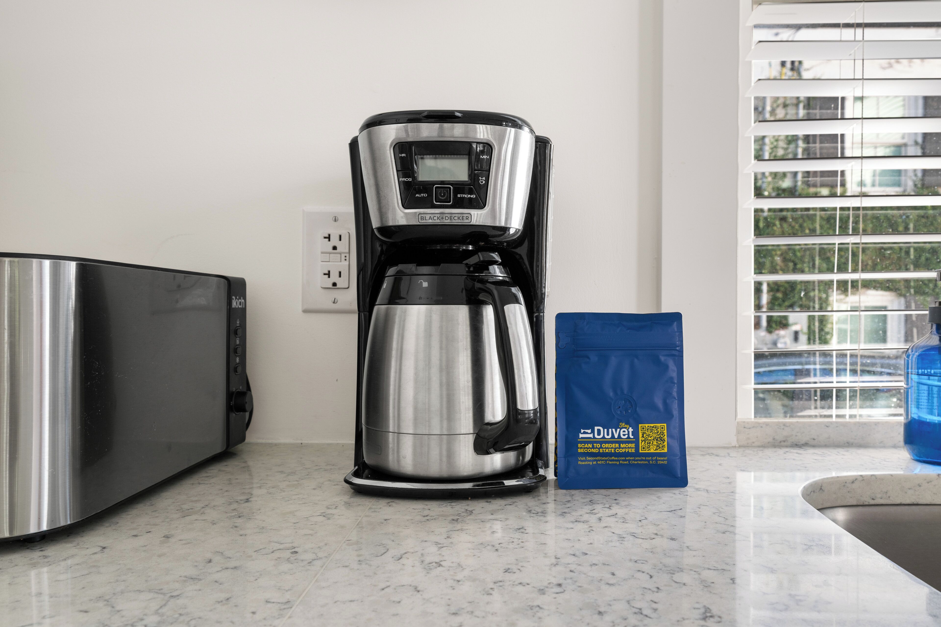 A kitchen with a coffee maker, a microwave, and a bag of Duvolt coffee.