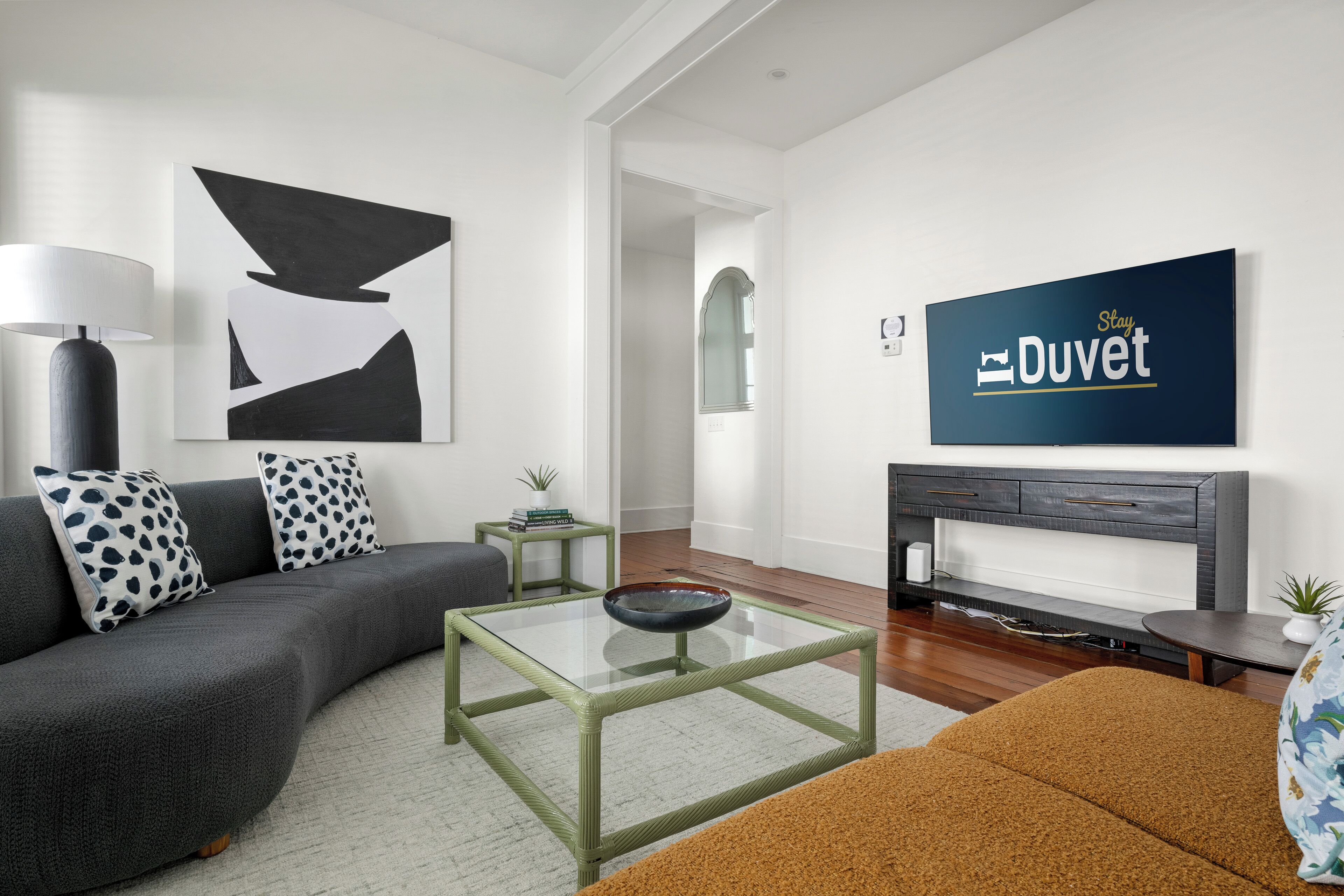 A modern living room with a grey sofa, a glass coffee table, and a flat-screen TV mounted on the wall.