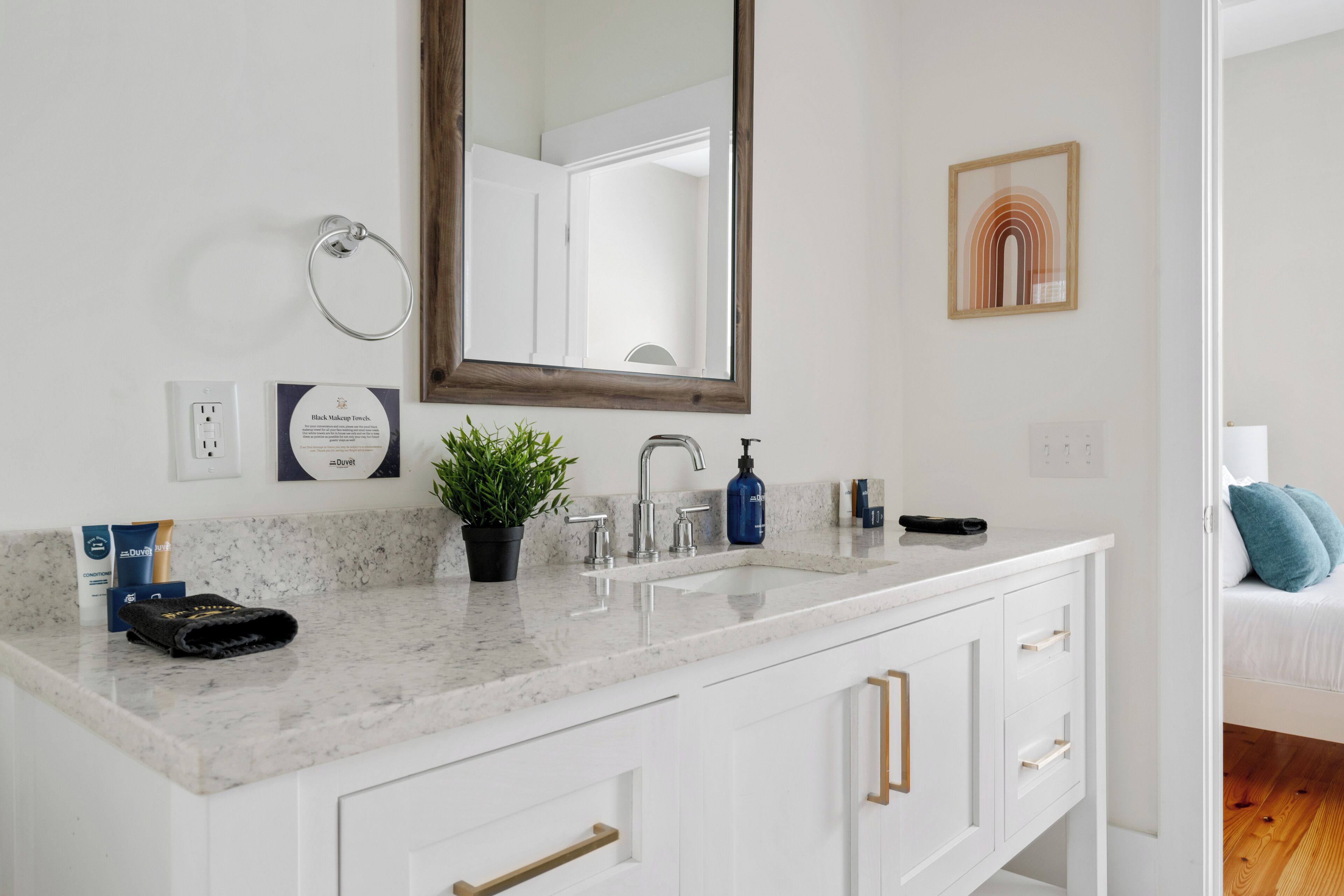 A bathroom with a white vanity, a mirror, a potted plant, a towel, and toiletries.