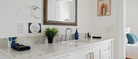 A bathroom with a white vanity, a mirror, a potted plant, a towel, and toiletries.