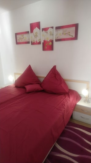 Een bed met rode beddengoed, een houten hoofdbord en twee bedlampjes.