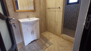 Une salle de bain avec un lavabo blanc, un miroir avec un cadre doré, des murs recouverts de carreaux beiges et un espace douche avec un mur de crédence en carreaux à motifs.