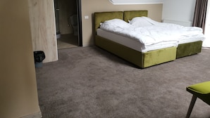Une chambre à coucher avec un lit, une tête de lit recouverte d’un tissu vert, un tapis gris et une fenêtre avec des rideaux.