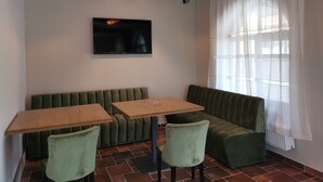 Un espace repas moderne avec un coin salon vert, deux tables en bois et un téléviseur fixé au mur.