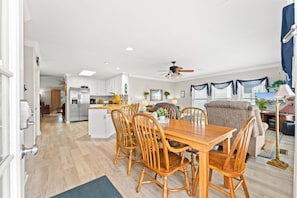A spacious living area with a dining table and chairs, a kitchen in the background, and a view of a pool through the windows. - Channel Cat - Gorgeous Cherry Grove Channel House with Pool (North Myrtle Beach)