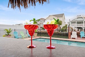 Two red cocktail glasses with flowers and mint leaves on a poolside table. - Channel Cat - Gorgeous Cherry Grove Channel House with Pool (North Myrtle Beach)