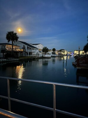 A waterfront property with a dock, a bridge, and a calm body of water reflecting the moonlight. - Channel Cat - Gorgeous Cherry Grove Channel House with Pool (North Myrtle Beach)