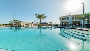 A clear blue pool with lounge chairs and palm trees, surrounded by buildings with large windows and a sunny sky.