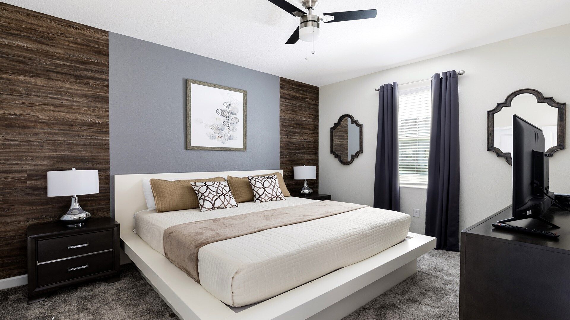 A bedroom with a bed, nightstands, a ceiling fan, a large mirror, and a window with curtains.