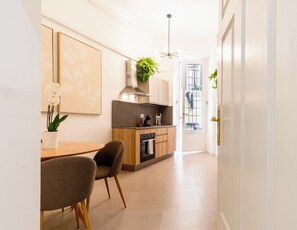 Una cocina moderna con comedor, que cuenta con una isla central, armarios de madera y una lámpara colgante.