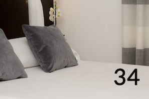 A bed with two grey pillows and a white mattress, a white orchid plant, and a number '34' in the corner.