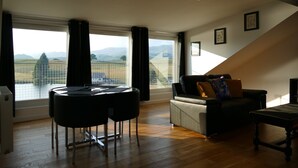 A modern living room with a dining area, large windows with a view of the countryside, and a loft-style ceiling. - The Annexe at Loch View Farm will take your breath away (Crieff)