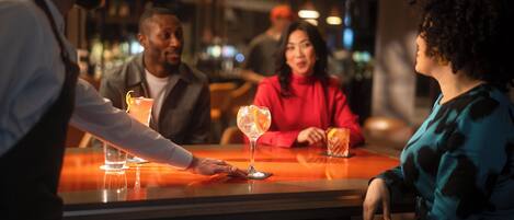 A bar area with a bartender serving drinks to customers seated at a table.