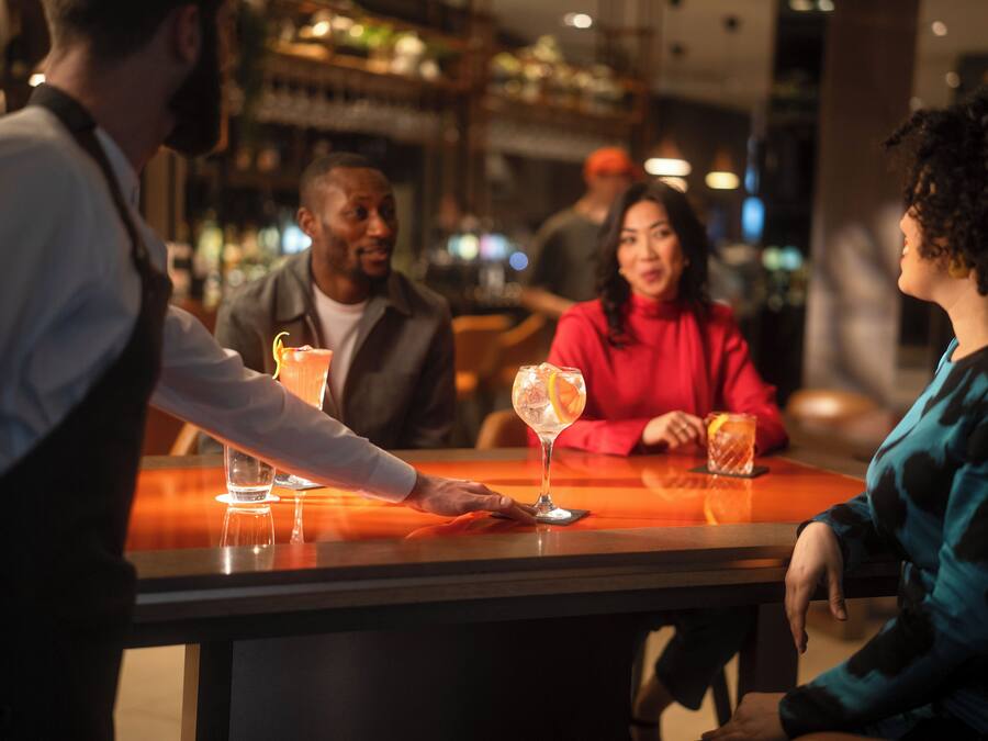A bar area with a bartender serving drinks to customers seated at a table.