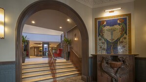 Une entrée imposante, avec une grande arche, un escalier et un mur décoratif orné d’une fresque.