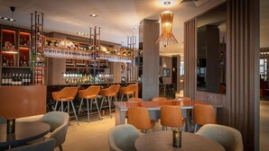 Un espace bar offrant différentes options de sièges, notamment des tabourets et des tables, ainsi qu’une variété de bouteilles et de verres exposés sur des étagères.