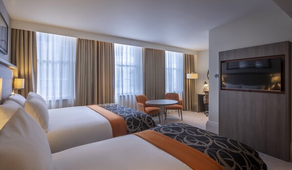 Ein Hotelzimmer mit zwei Betten, einem kleinen runden Tisch und einem an der Wand befestigten Fernseher.