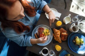 Eine Person genießt ein Frühstück am Tisch, mit Croissants, Eiern und einer Teller Wurst.