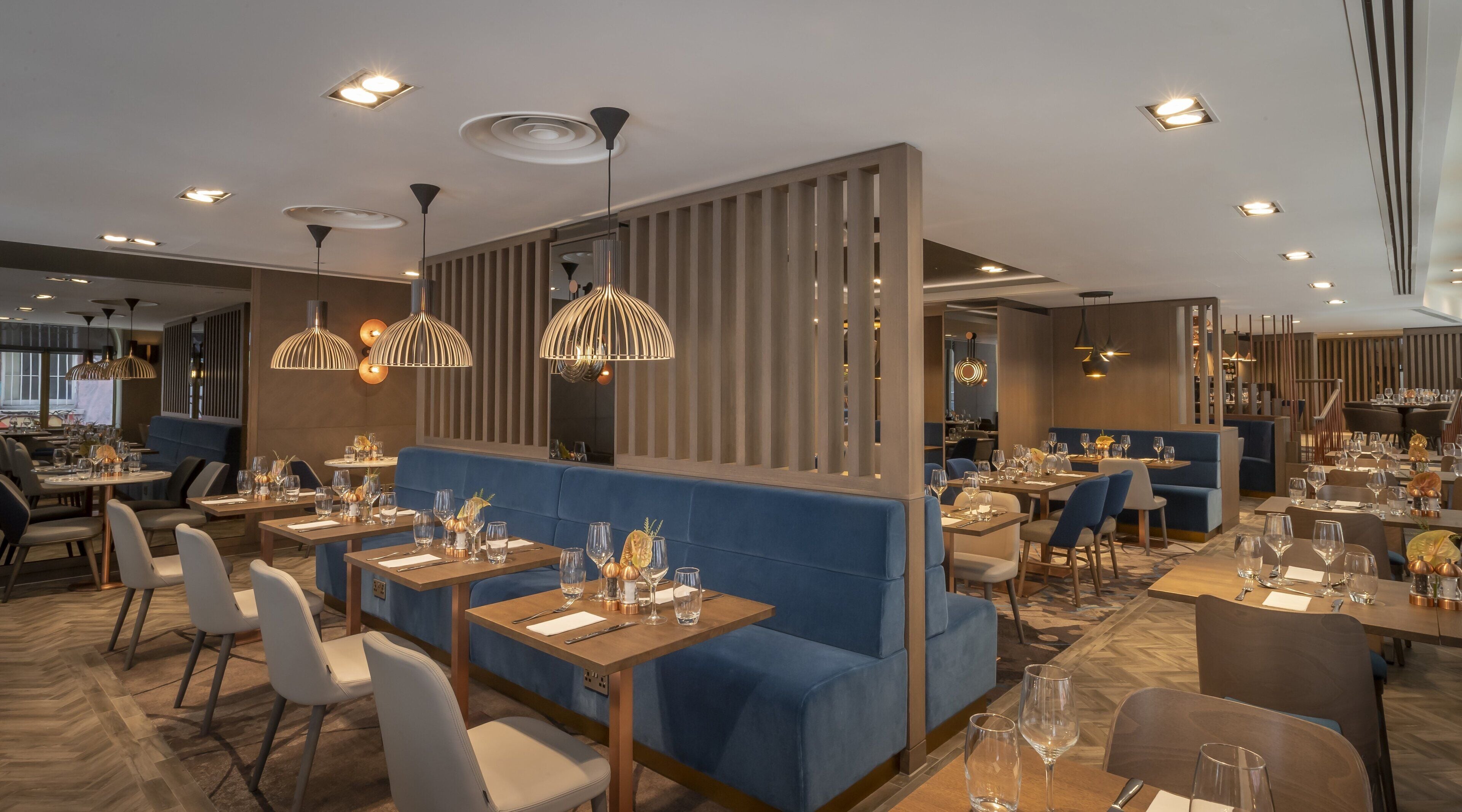 Un restaurant moderne avec des sièges rembourrés bleus, des tables en bois et des luminaires suspendus.