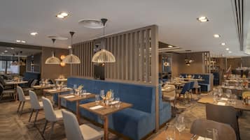 A modern restaurant with blue cushioned seating, wooden tables, and pendant lighting.