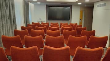 A conference room with rows of orange chairs, a large screen, and recessed ceiling lighting.
