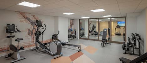 A gym with cardio machines, free weights, and a mirrored wall.