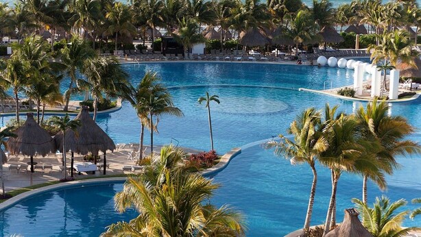 A resort with a large infinity pool, palm trees, and a view of the ocean. - Vidanta Mayan Palace 2 bedroom 2 Bath  (Riveria Maya)