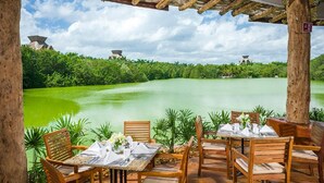 An outdoor dining area with wooden tables and chairs, overlooking a calm river and lush greenery. - Vidanta Mayan Palace 2 bedroom 2 Bath  (Riveria Maya)