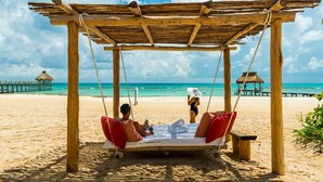 A wooden swing bed with red cushions on a sandy beach, overlooking the ocean. - Vidanta Mayan Palace 2 bedroom 2 Bath  (Riveria Maya)