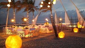 An outdoor dining area with tables set for a meal, palm trees, and decorative lights. - Mayan Palace Acapulco (Acapulco, Guerrero)