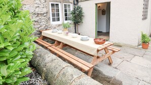 Un edificio de piedra con una mesa y banco de madera en el exterior.