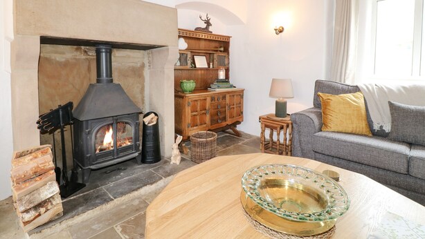 Una sala de estar acogedora con una chimenea de piedra, un mueble de madera, un sofá y una mesa con un cuenco decorativo.