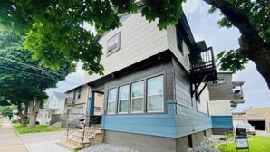 A two-story residential building with a blue exterior, a front porch, and a small front yard with gravel.