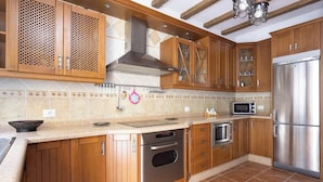 A kitchen with wooden cabinets, a stainless steel refrigerator, an oven, a microwave, and a hanging pot rack.
