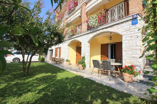 A building with a stone facade, multiple balconies with flower boxes, and outdoor seating with tables and chairs.