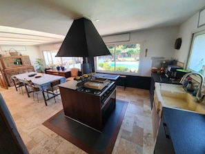 A modern kitchen with a central island, a dining area with a table and chairs, and a view of a swimming pool through large windows.