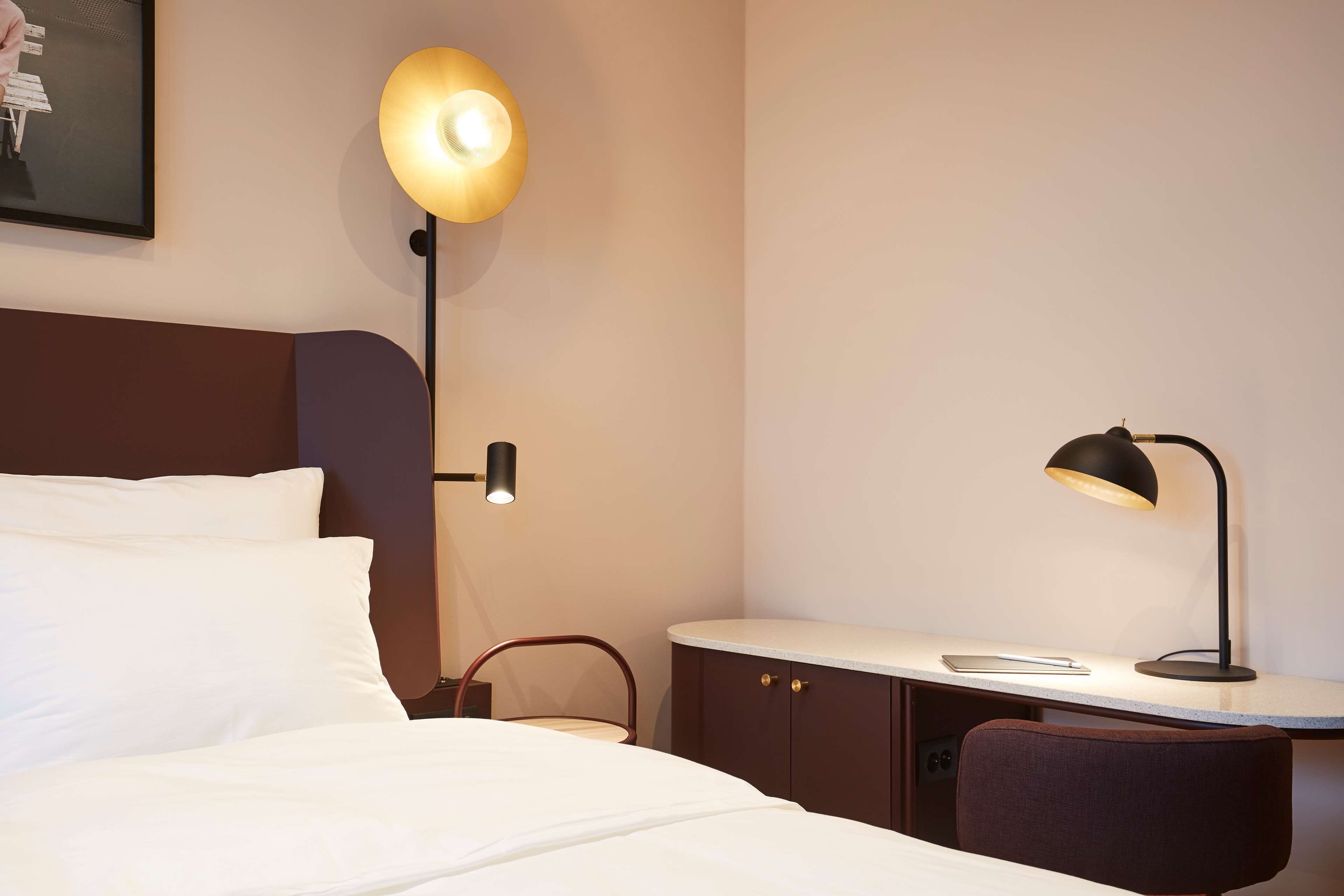 A hotel room with a bed, a desk, a chair, and two lamps.