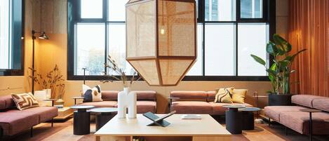 A modern interior with a large window, a geometric hanging light fixture, and a variety of seating arrangements.