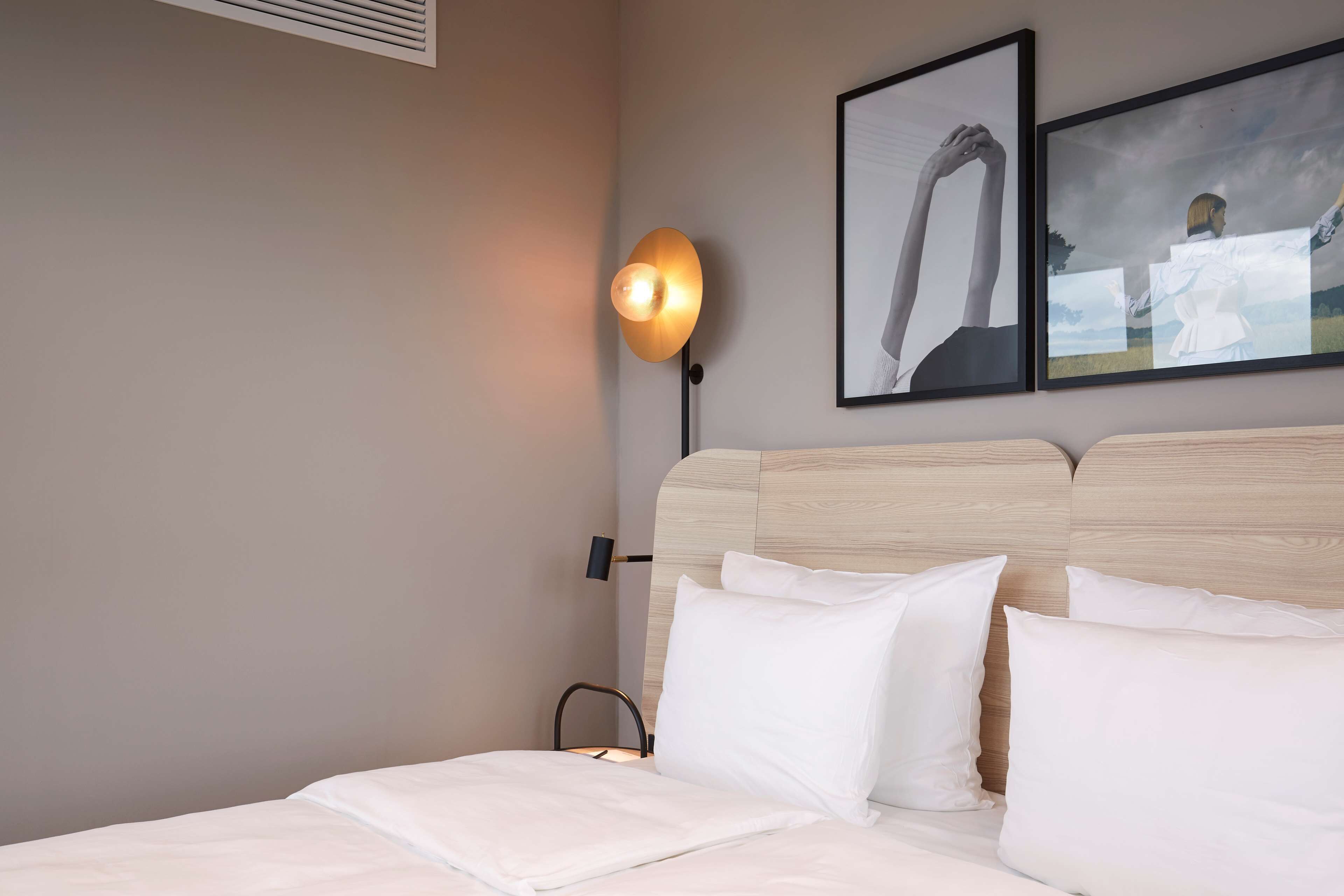 Ein Hotelzimmer mit Bett, Nachttisch, Wandlampe und zwei gerahmten Bildern an der Wand.