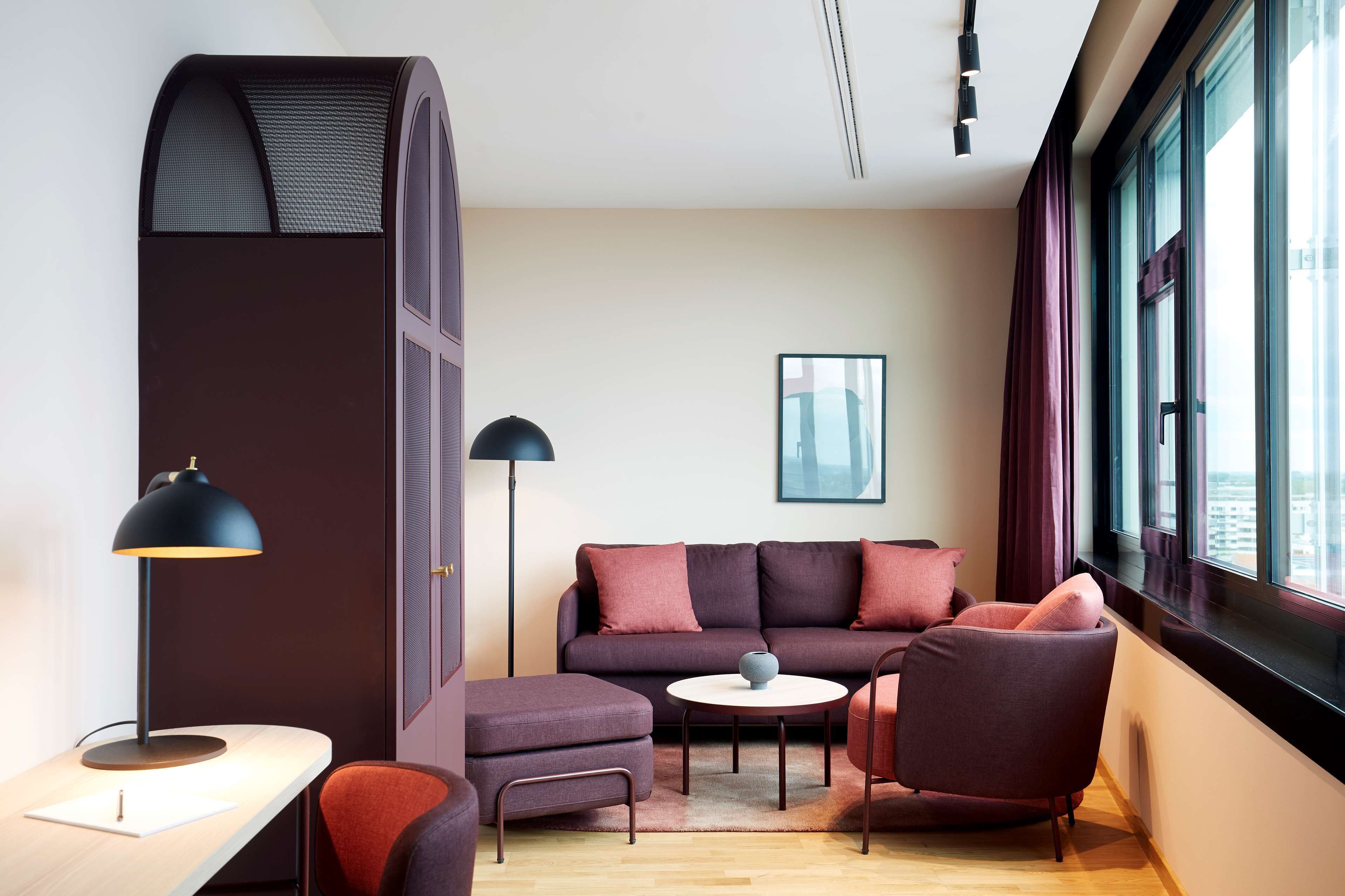 Uma sala de estar moderna com sofá, poltronas, uma mesinha e uma escrivaninha com abajur.