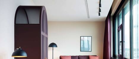 A modern living room with a sofa, armchairs, a small table, and a desk with a lamp.