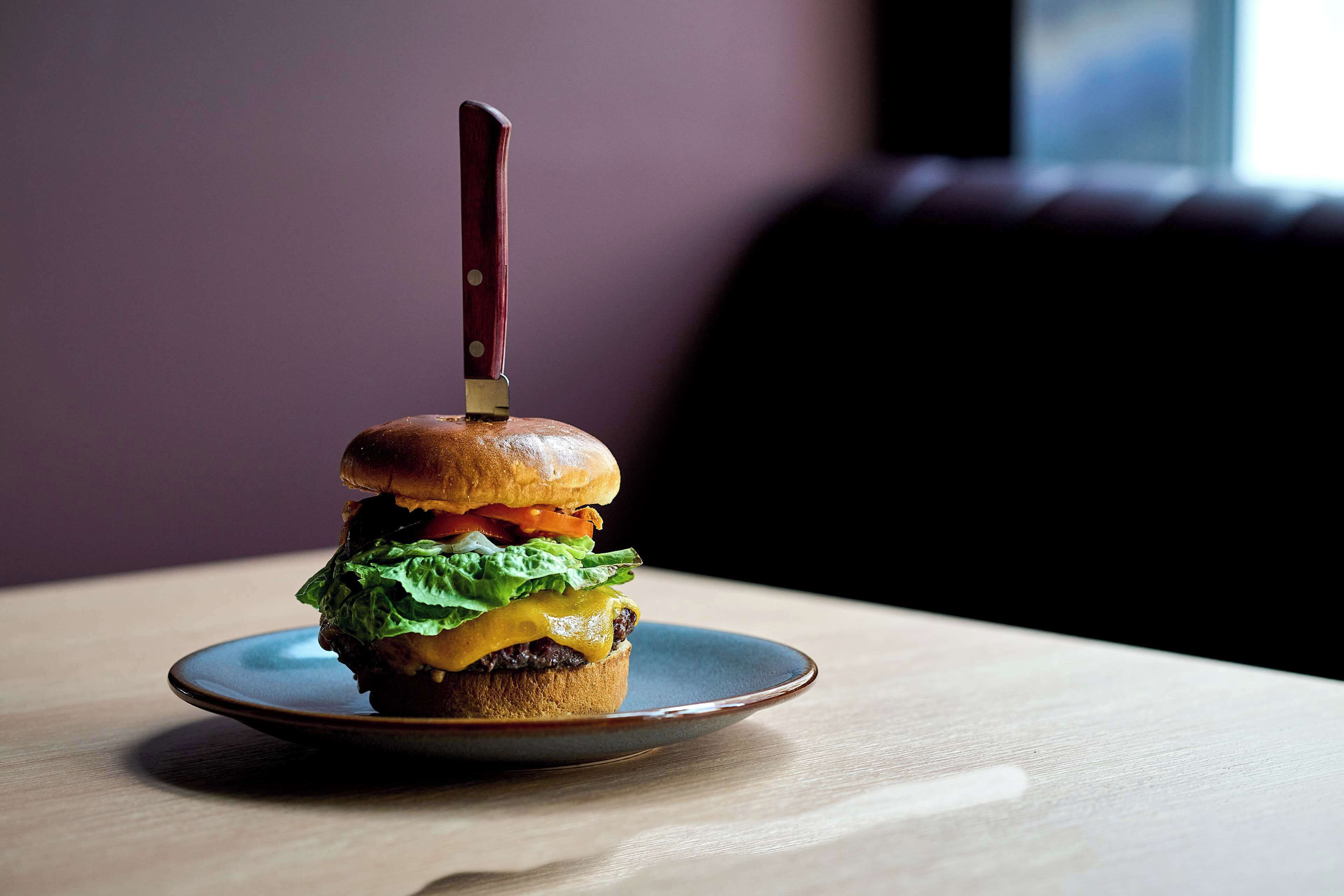 A burger on a plate with a knife on top, placed on a table.