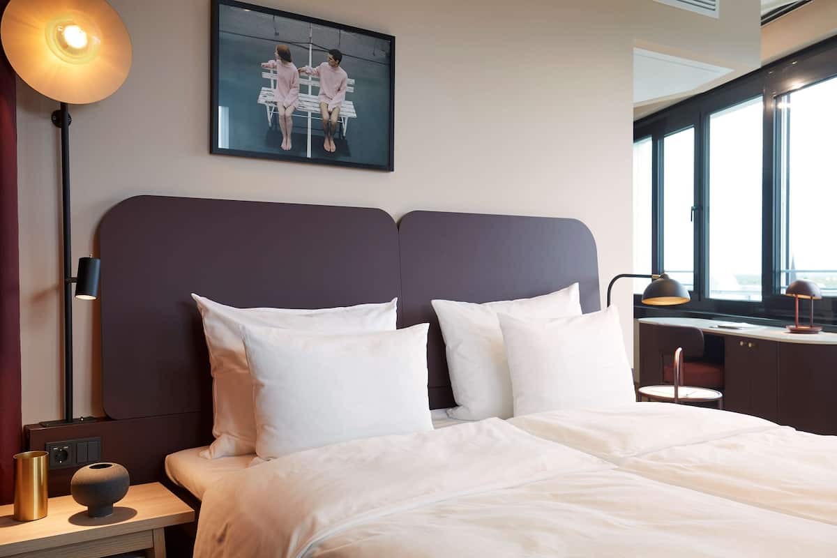 Moderni hotellihuone, jossa on suuri sänky, työpöytä ja ikkuna, josta on näkymä.