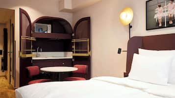 Habitación de hotel con cama, una pequeña mesa redonda con dos sillas, kitchenette con microondas y un televisor de pared.