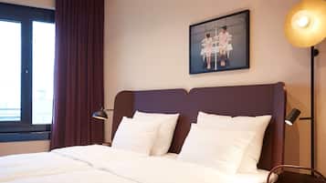 Habitación de hotel con una cama grande, cabecera, una obra de arte en la pared, lámpara de noche y una ventana con cortinas.