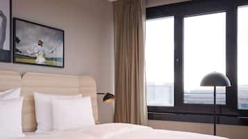 Une chambre d’hôtel avec un lit, une tête de lit, une fenêtre avec des rideaux, une lampe de sol et un tableau encadré au mur.